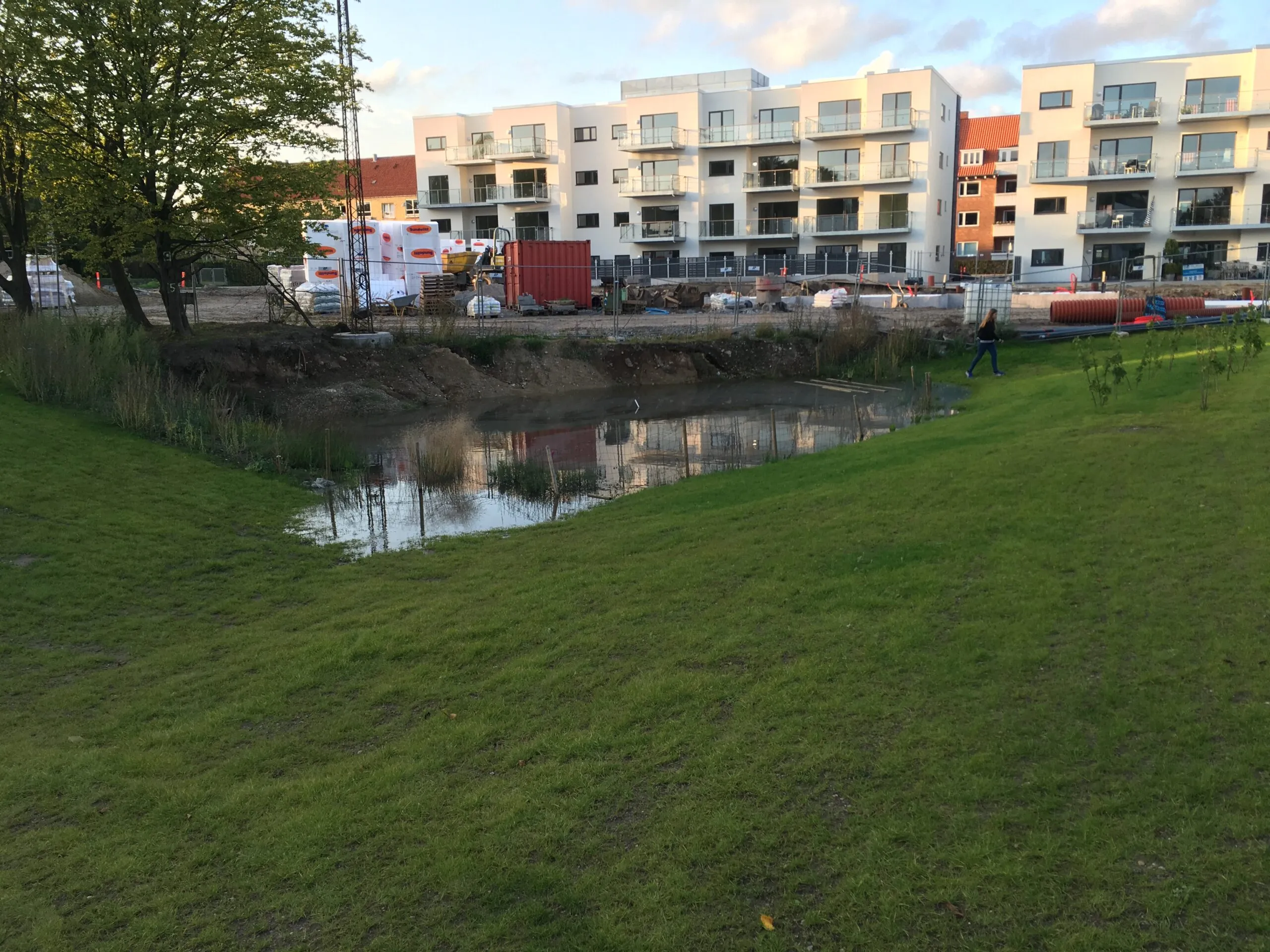 Regnvandsbassin foran lejlighedsbygning under opførelse med byggematerialer og containere på pladsen