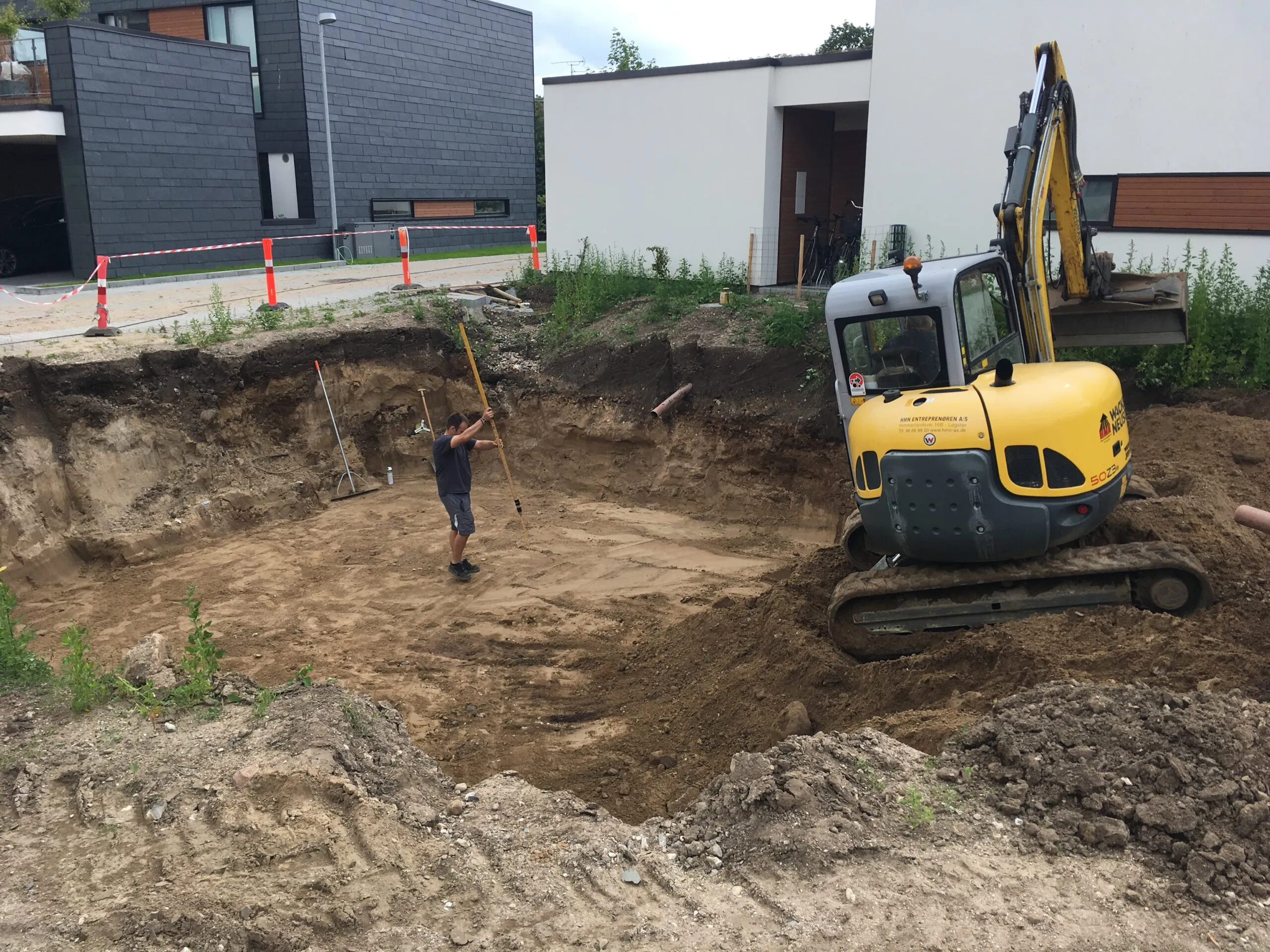 Udgravning med minigraver og arbejder i stort jordudgravningshul foran rækkehuse